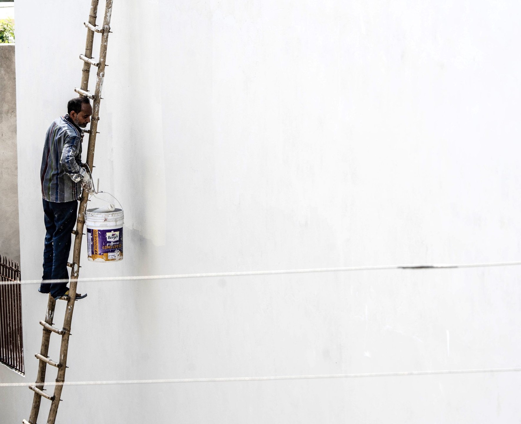 Painter working on a large wall from a ladder during exterior painting works
